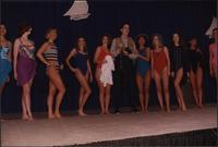 Ten Stevens models stand in a line in one-piece swimsuits with a male model in fishing gear during the Boat Show Fashion Show